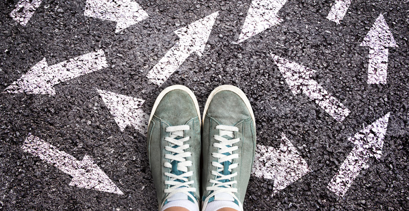 Looking down on two feet wearing trainers standing on a pavement with arrows drawn